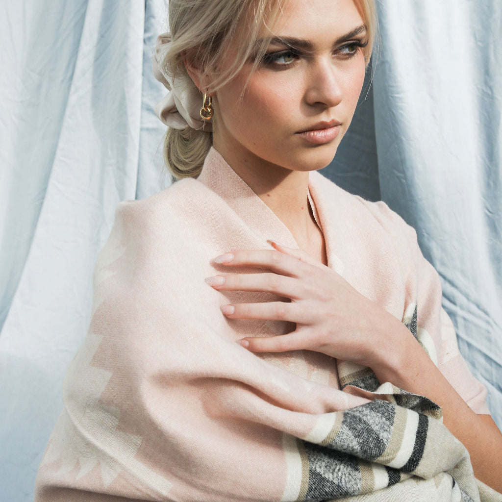 Woman wearing a light pink scarf with a patterned edge against a neutral background