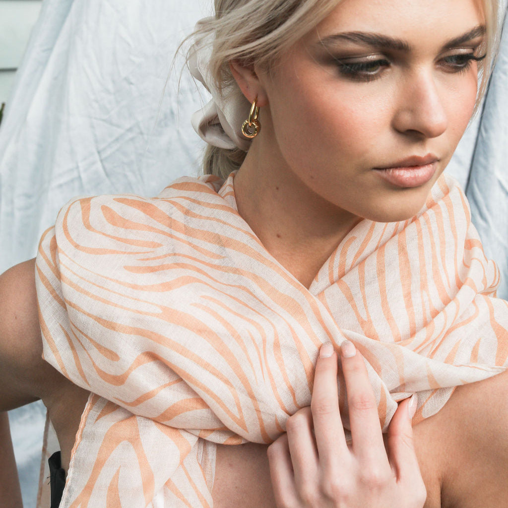 Woman wearing a bronze animal print and white patterned scarf with a blurred background