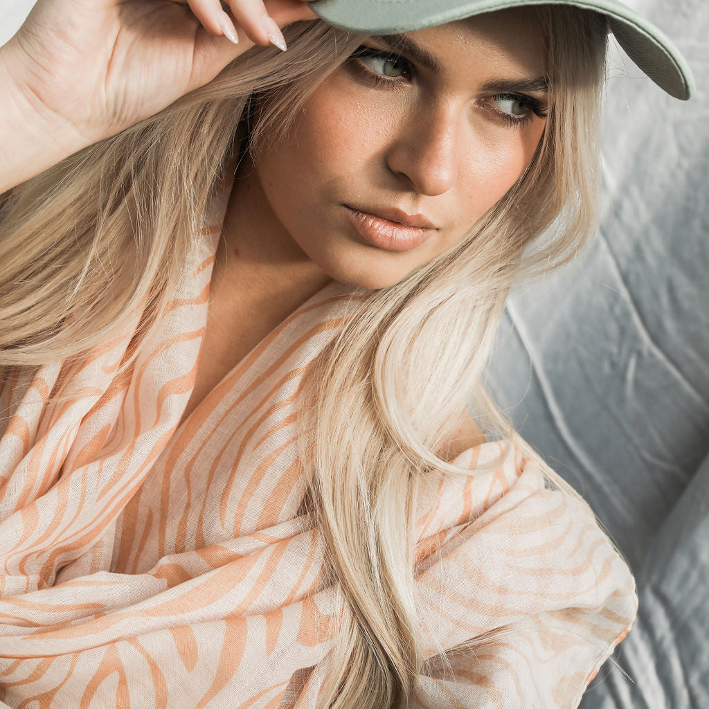Woman wearing a light-colored cap, animal print scarf with a neutral background