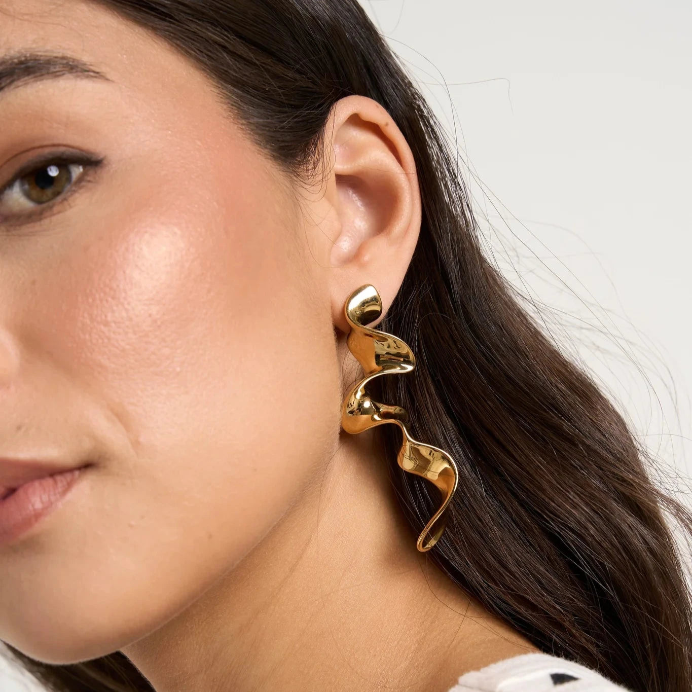 Close-up of a woman wearing gold Queen of the Foxes gold earrings with a neutral background