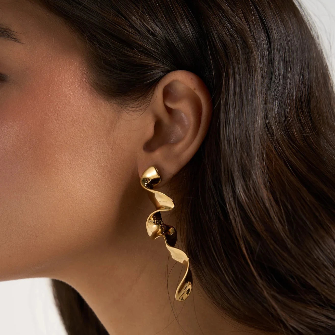 Close-up of  Queen of the Foxes gold ribbon earring worn by a person with a neutral background