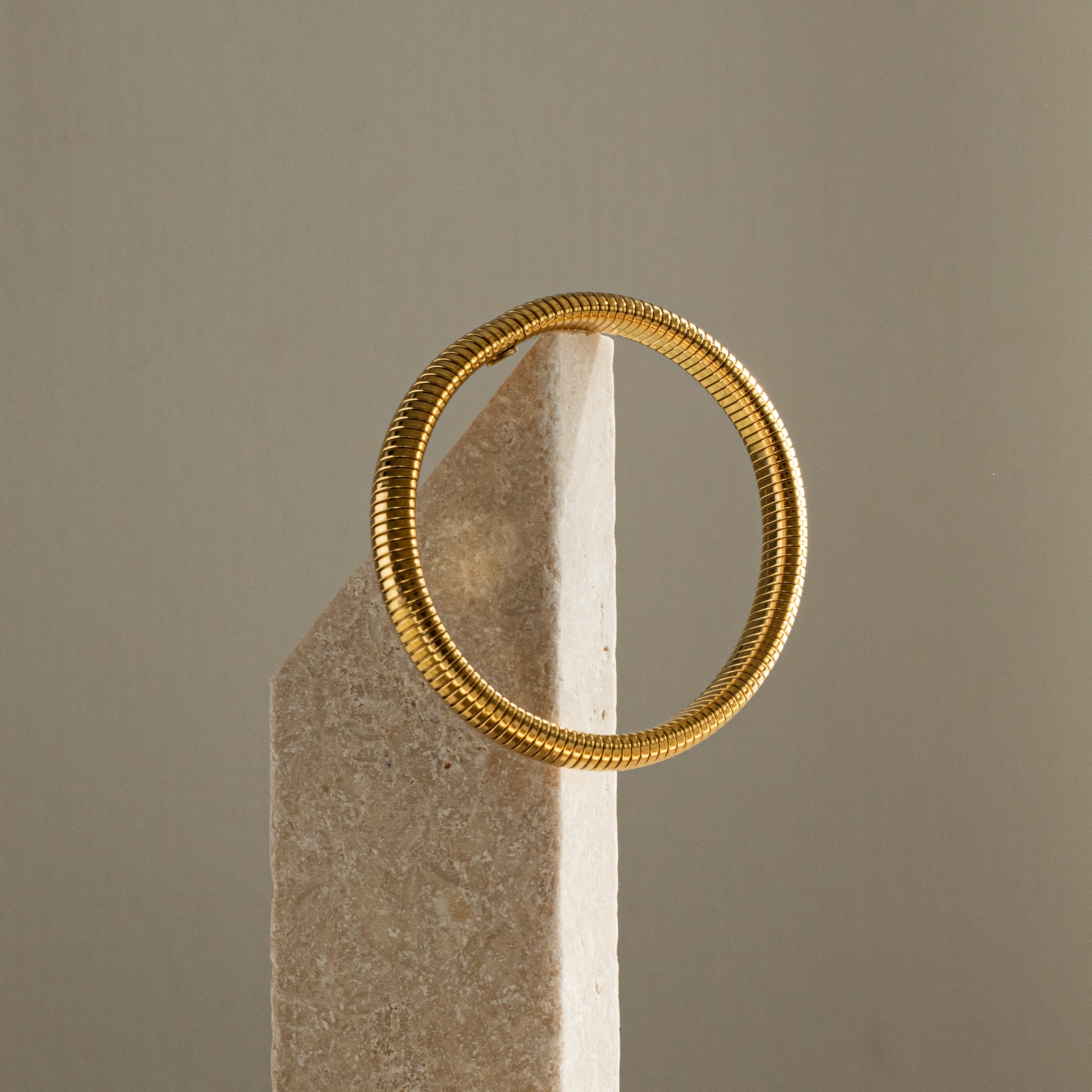 Gold bracelet on a stone block against a neutral background