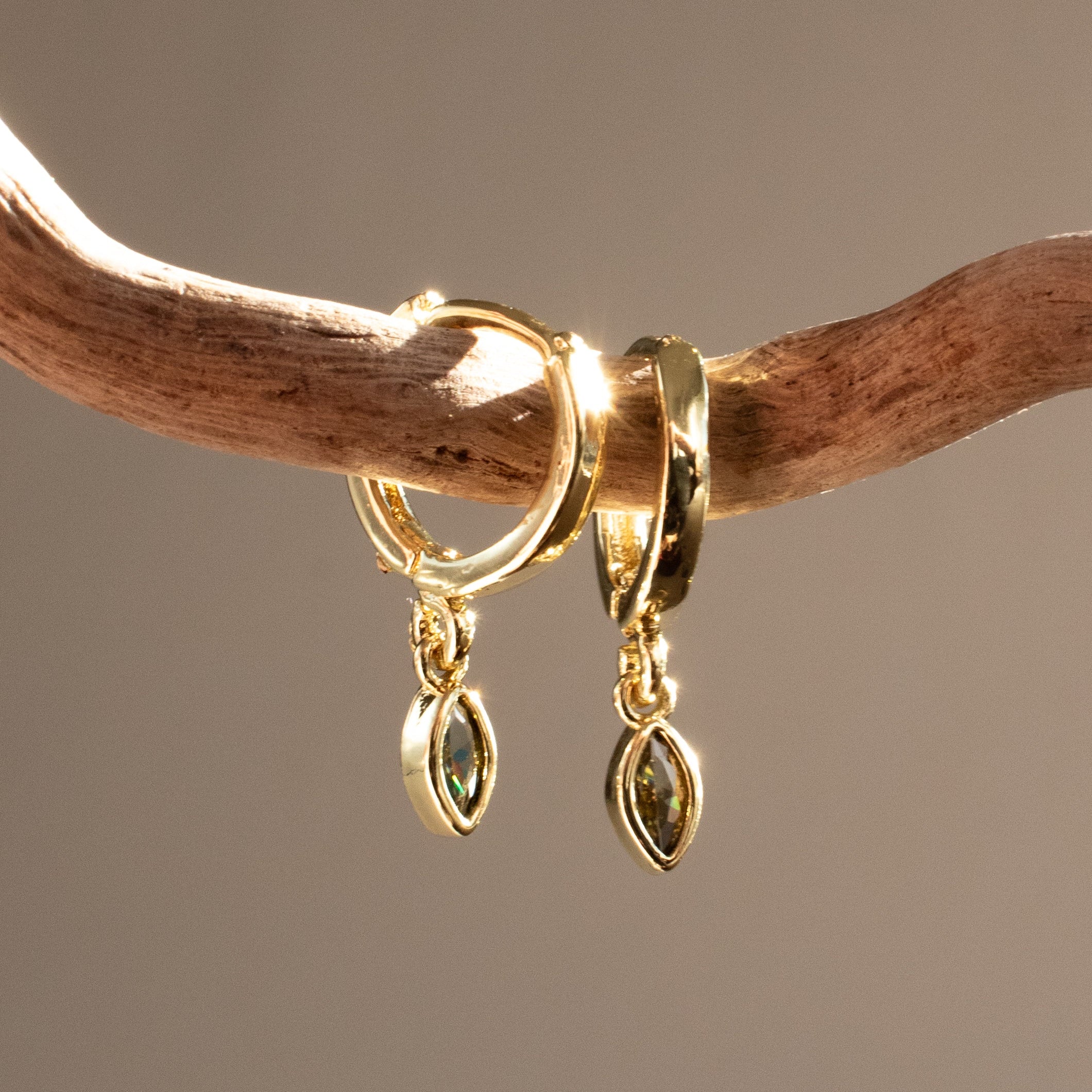 Gold sleeper earrings with marquise-shaped peridot gemstones on a wooden branch.