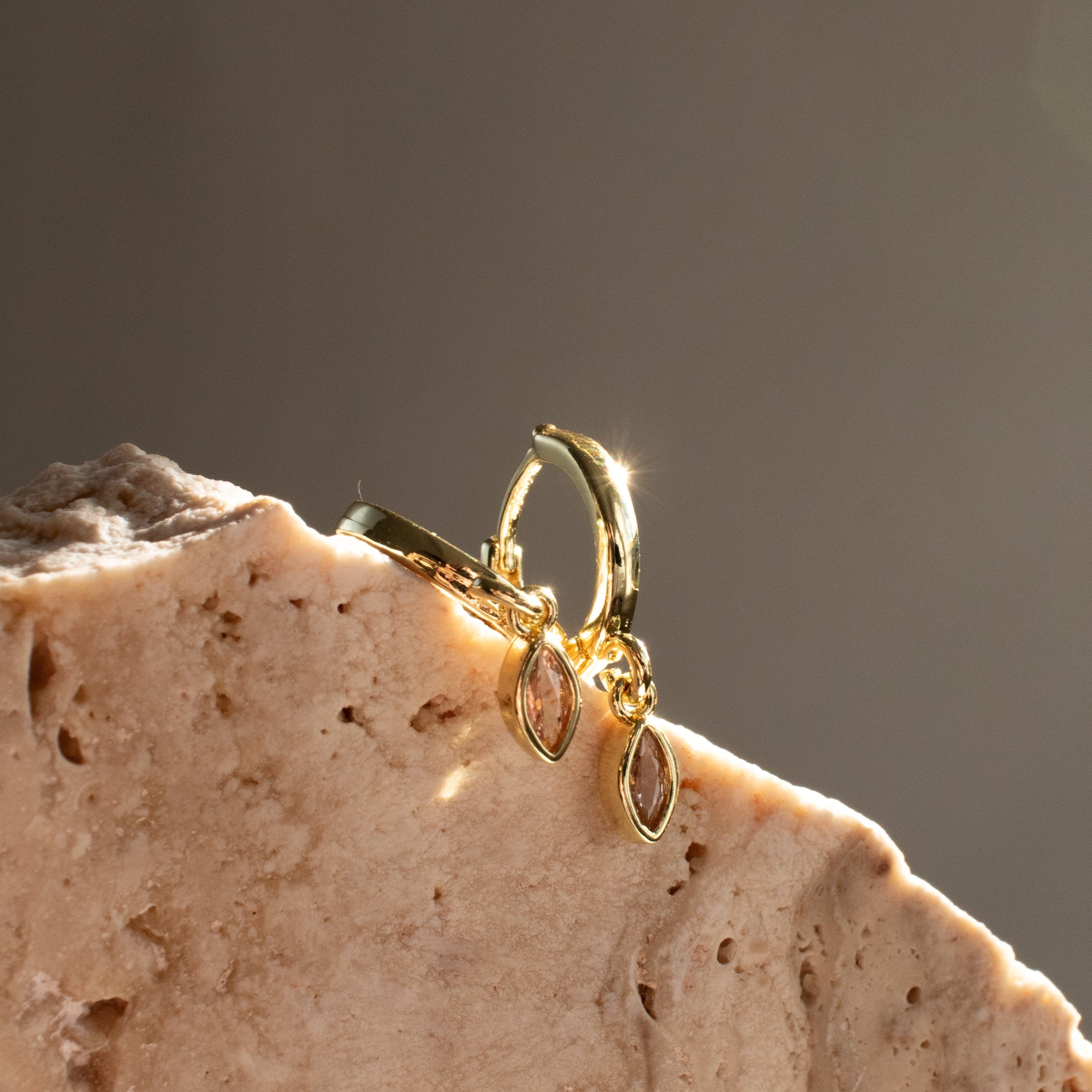Gold sleeper earrings with diamond marquise shaped stones on a textured stone surface with a dark background