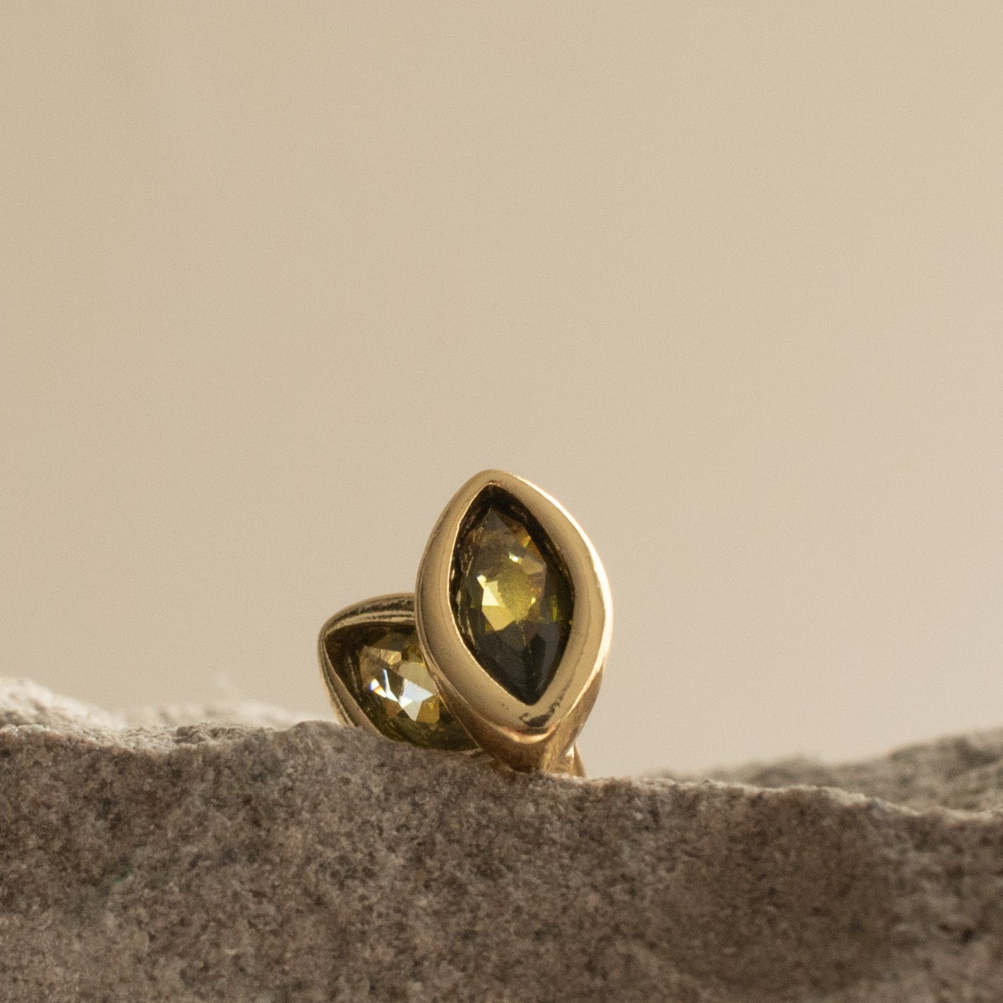 Gold marquise earrings with a peridot  gemstone on a textured surface