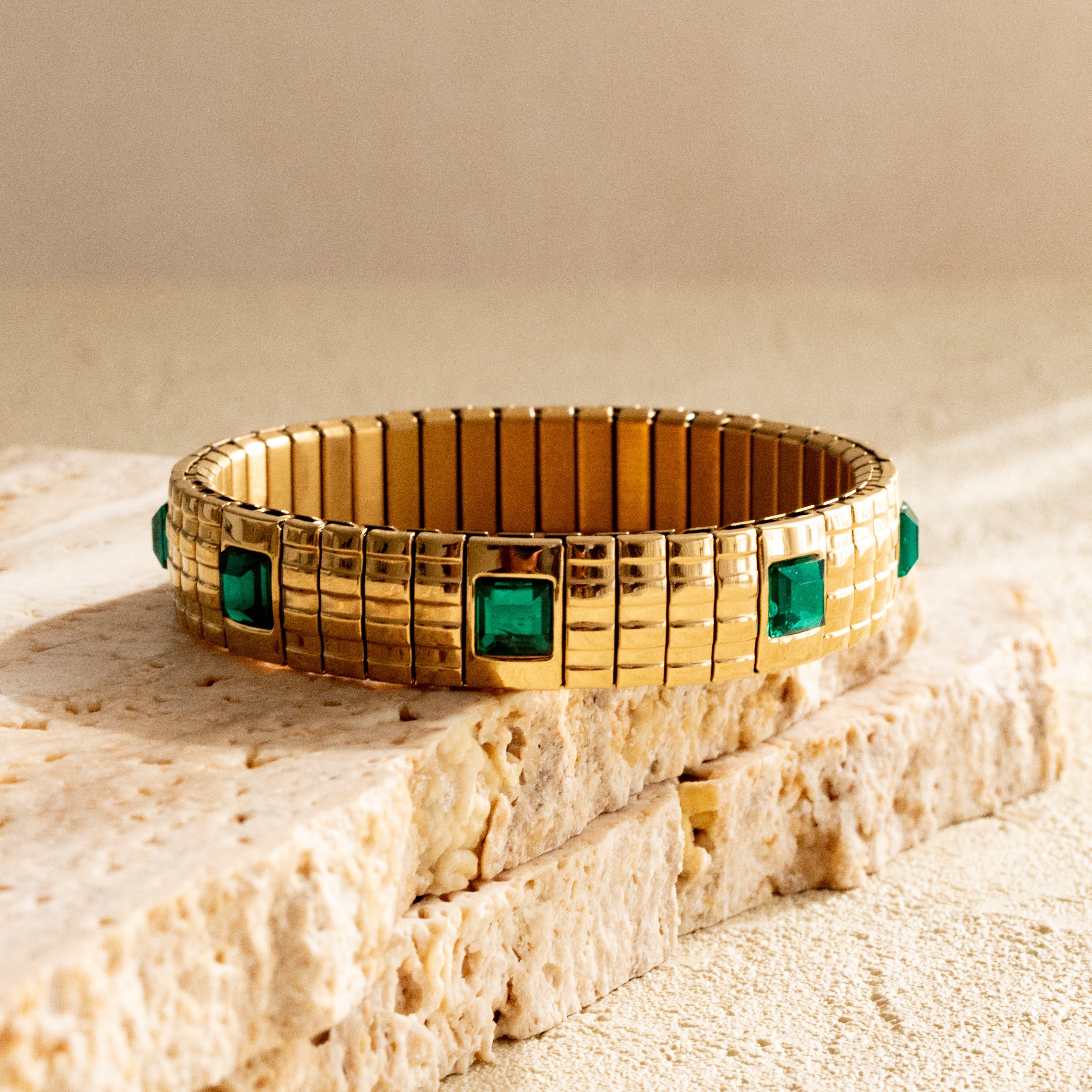 Gold strap bracelet with green gemstones on a textured beige surface