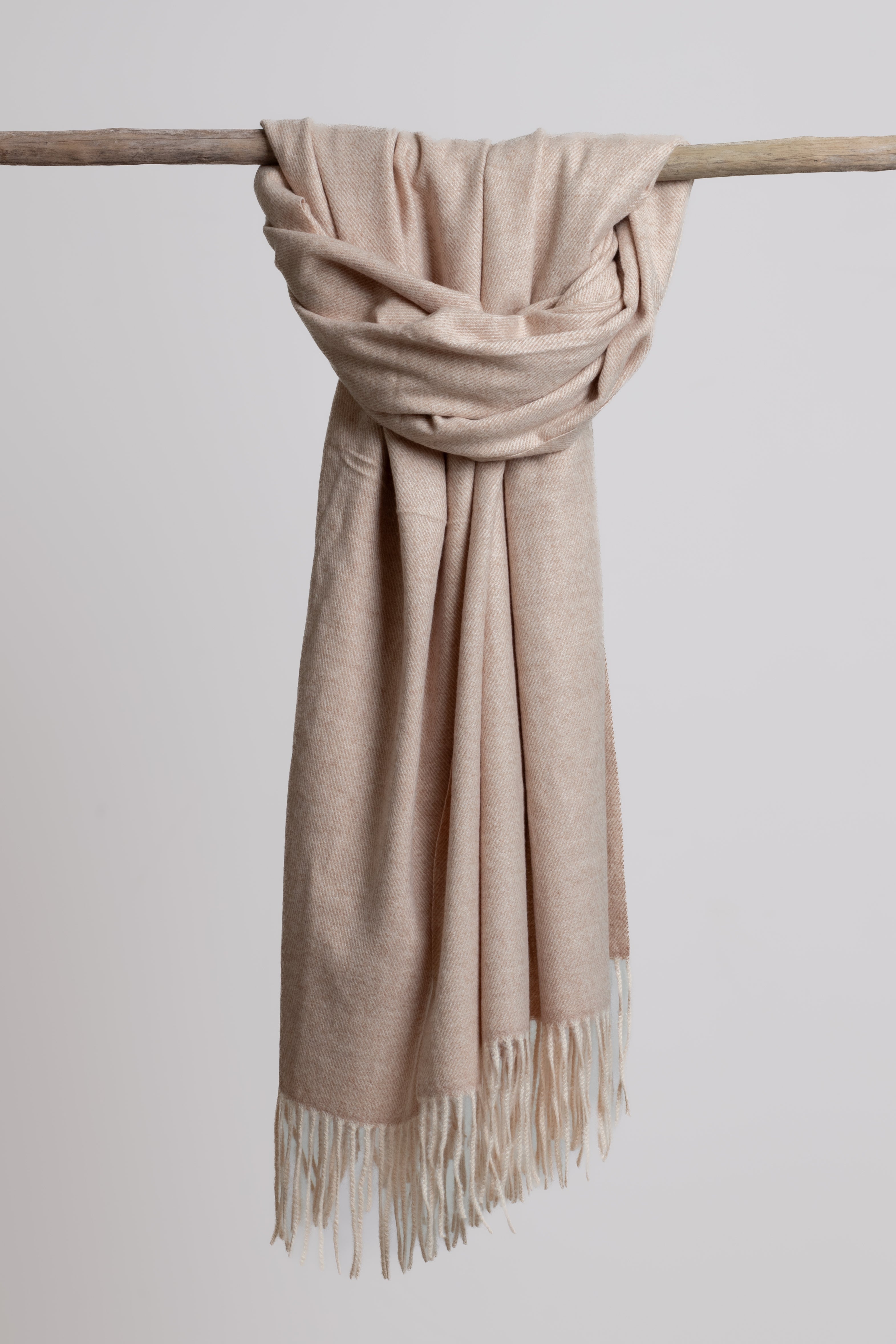 Creamy beige scarf with fringe draped over a branch against a light background