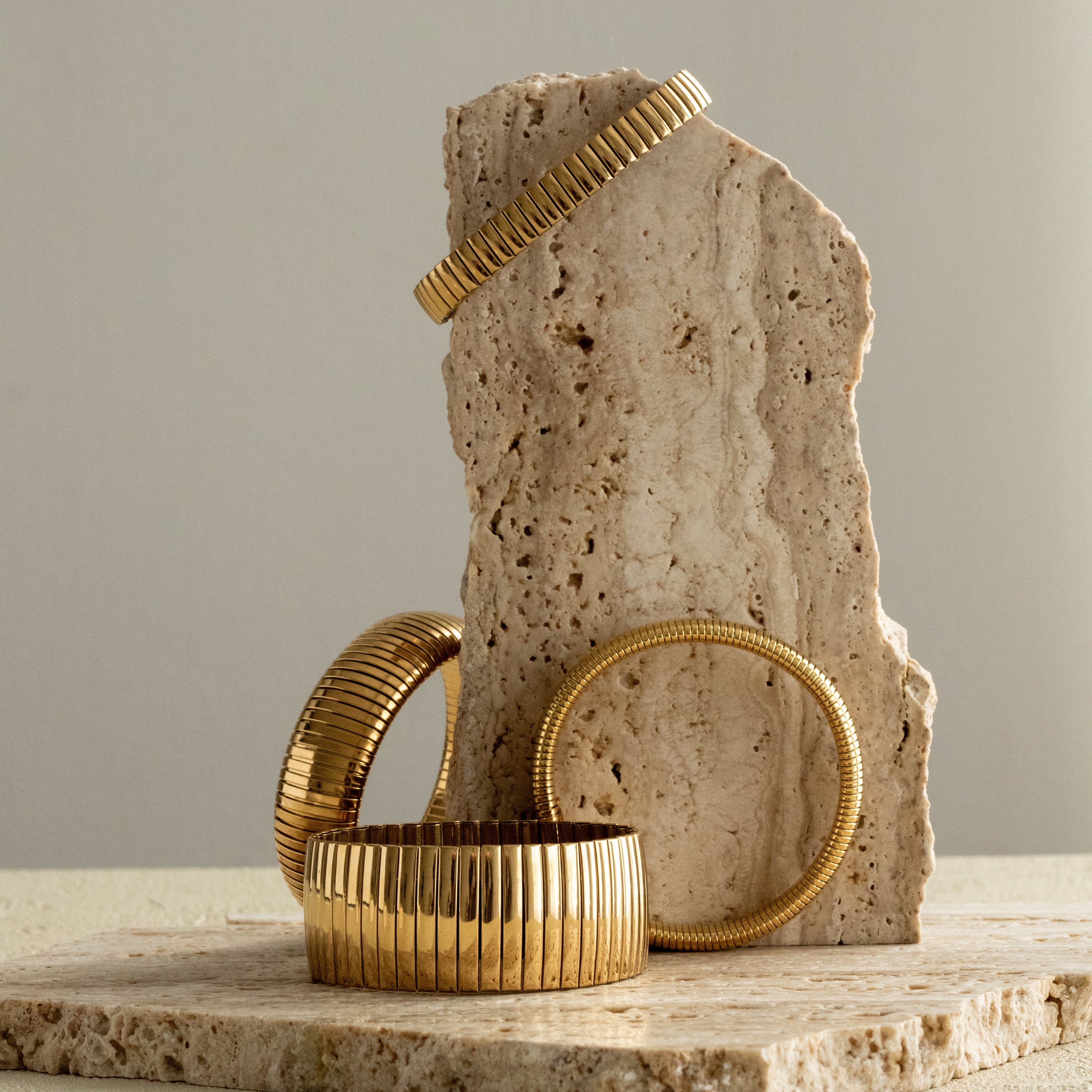 Gold banded and strap bracelets on a stone surface with a neutral background