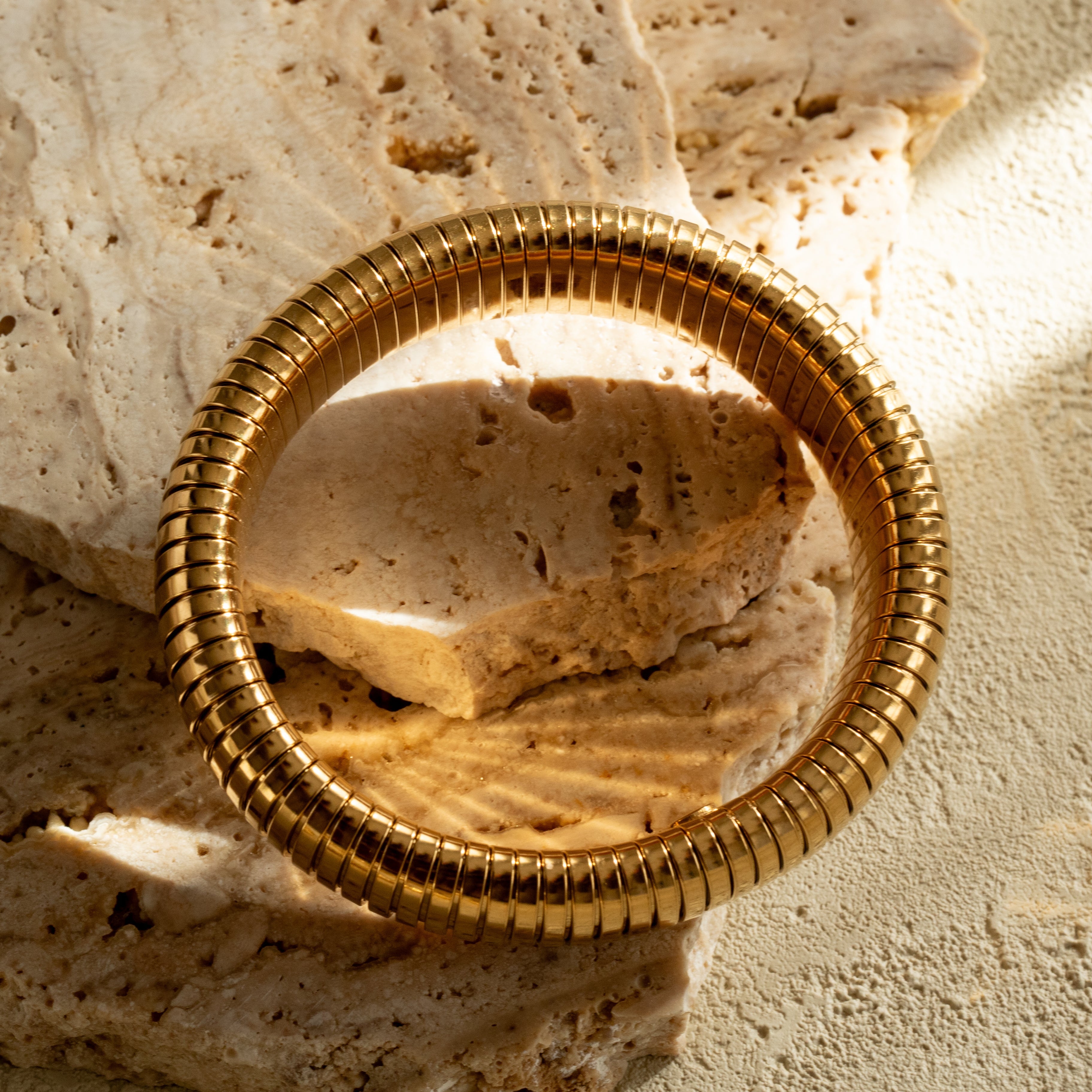 Wide gold banded bracelet  on a textured stone surface