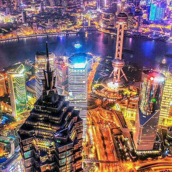 Aerial view of a cityscape at night with illuminated skyscrapers and a river.