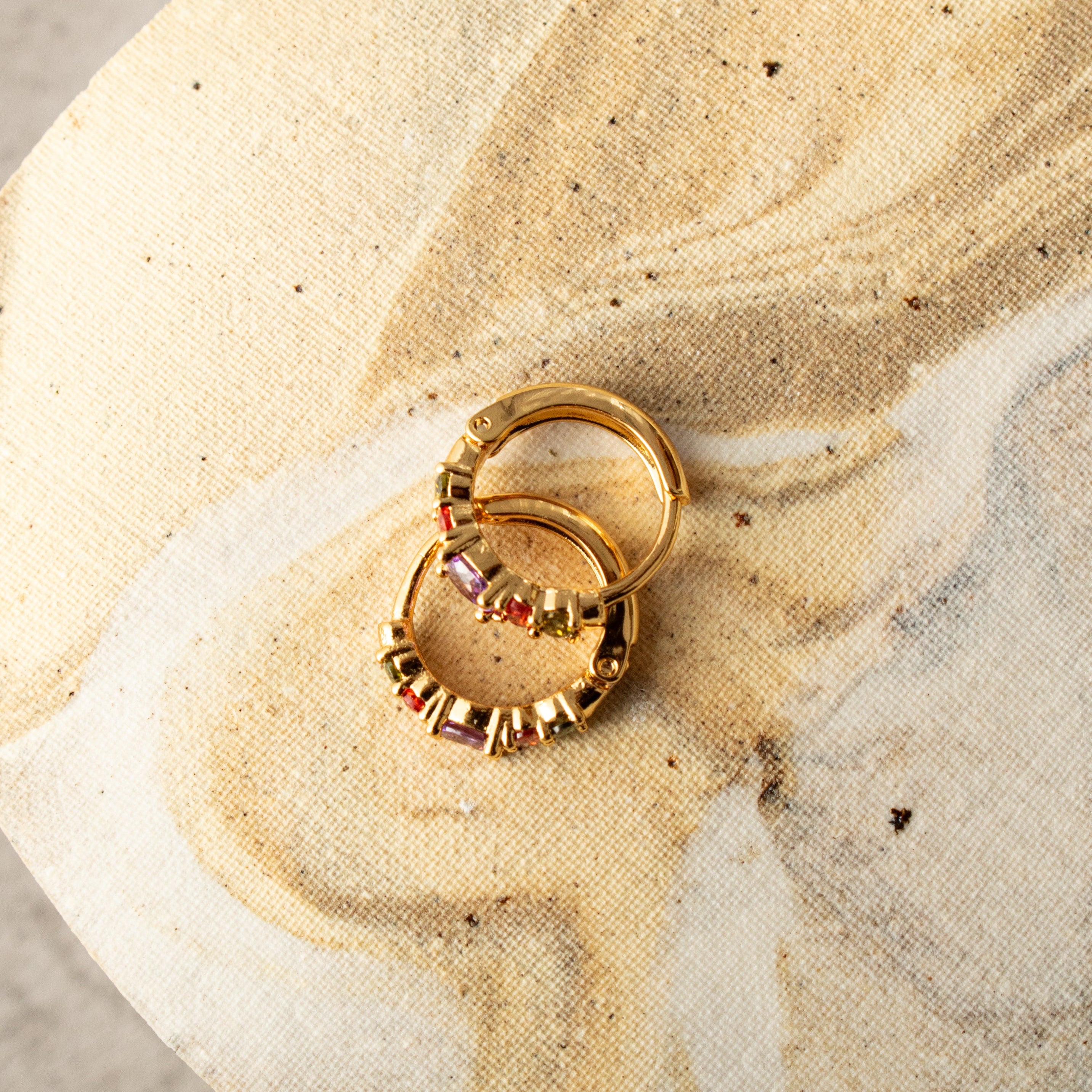 Gold earrings with stones on a textured beige surface