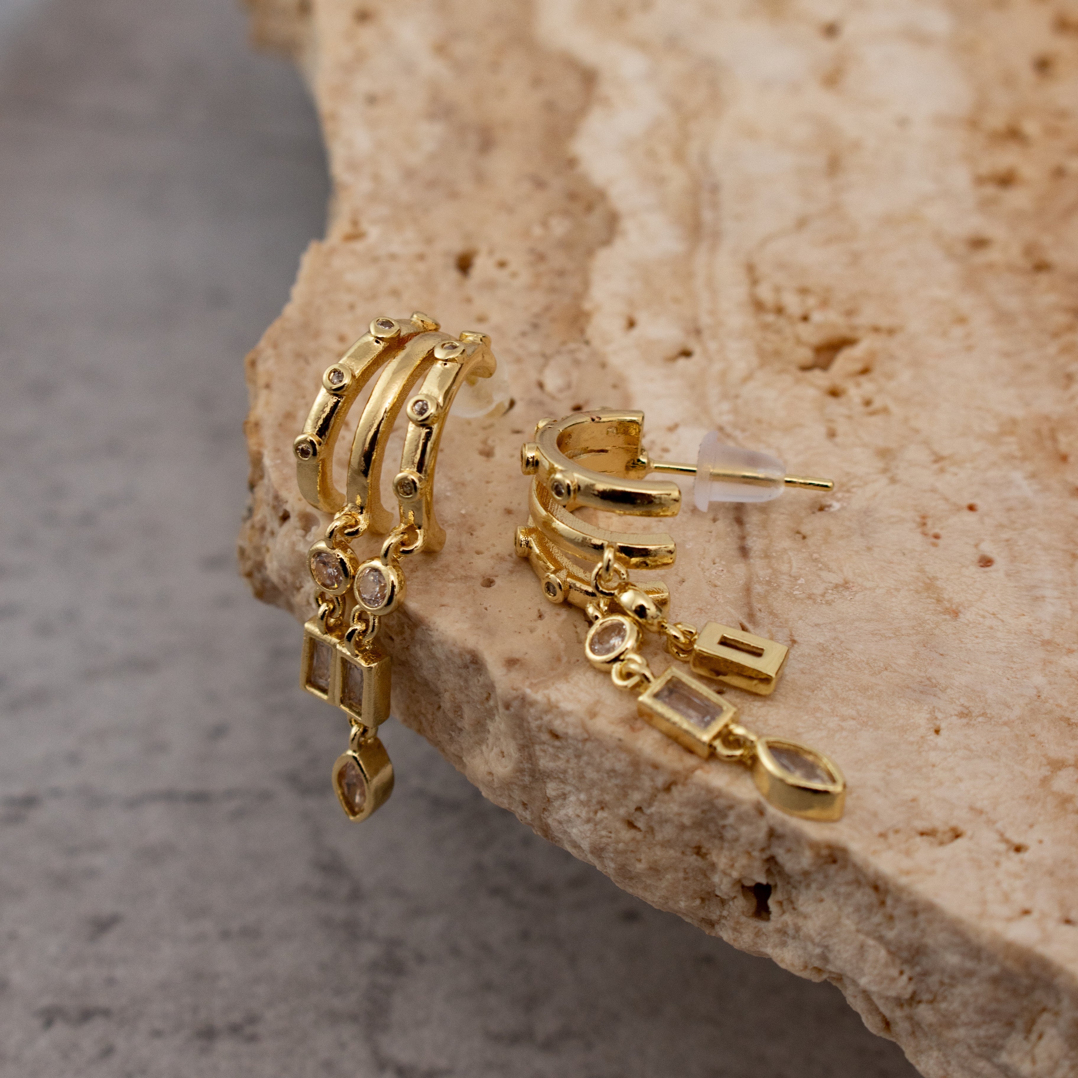 Gold hoop earrings with dangling charms on a textured stone surface