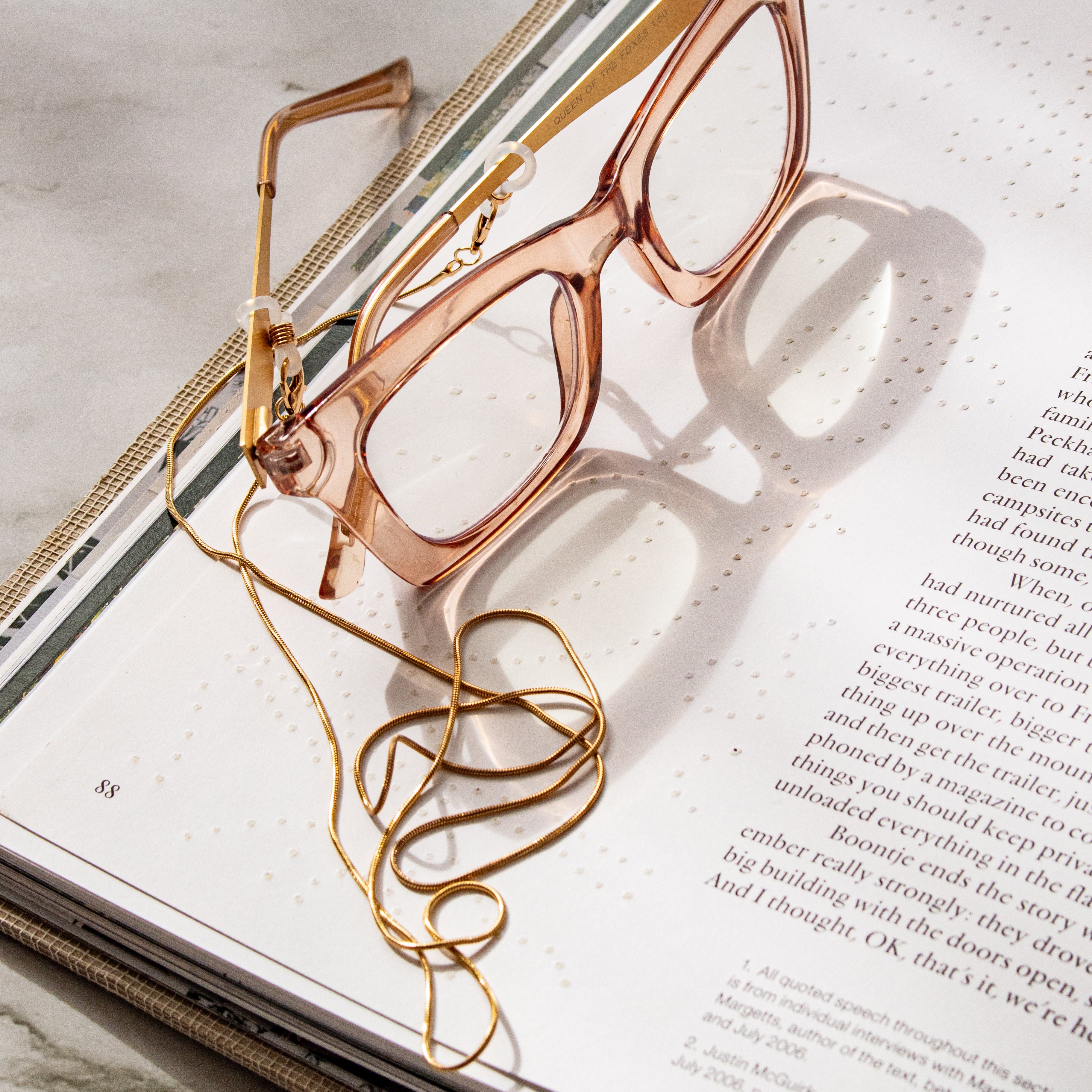 Rose gold eyeglasses with chain on an open book with a marble background
