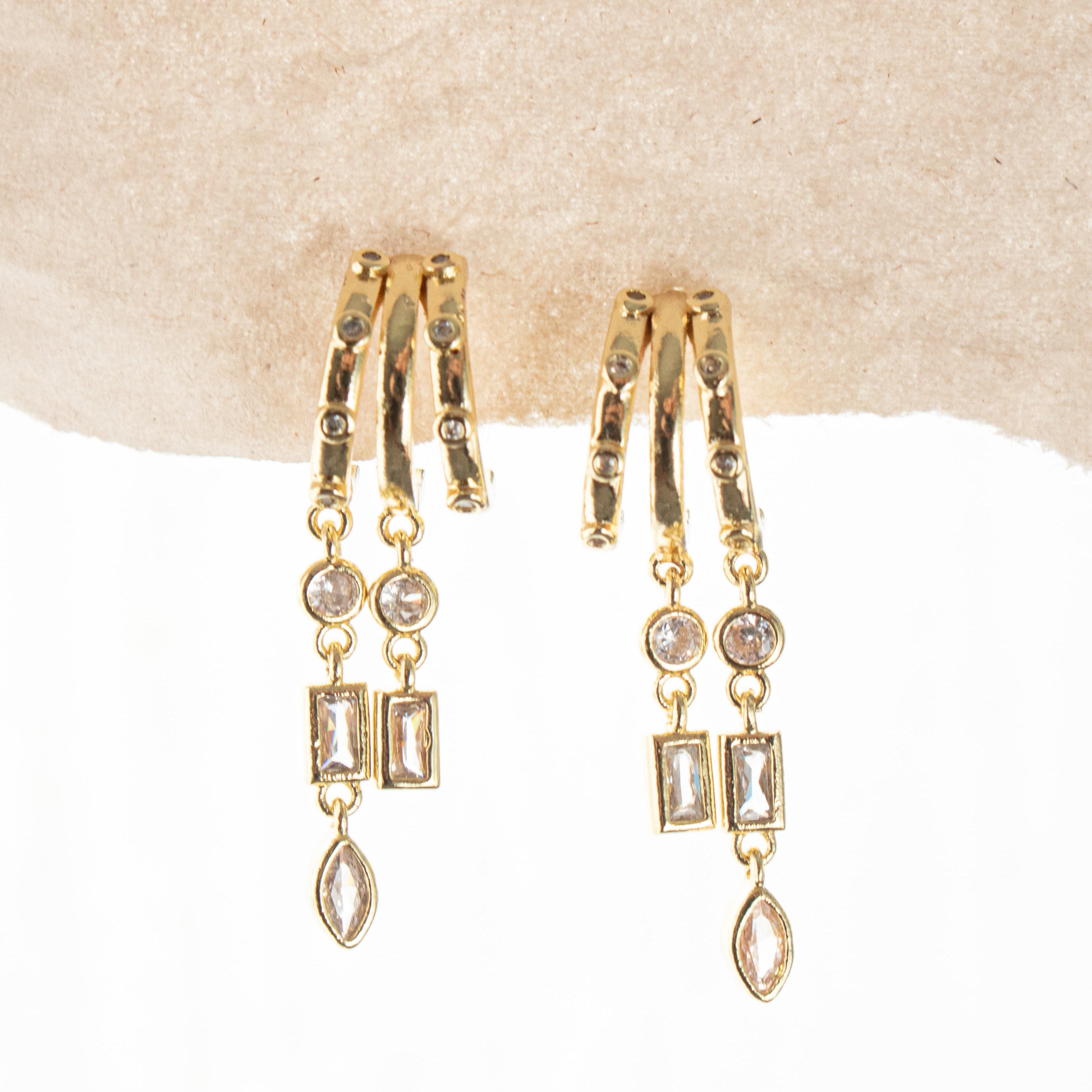 Gold hoop earrings with dangling gemstones on a beige surface