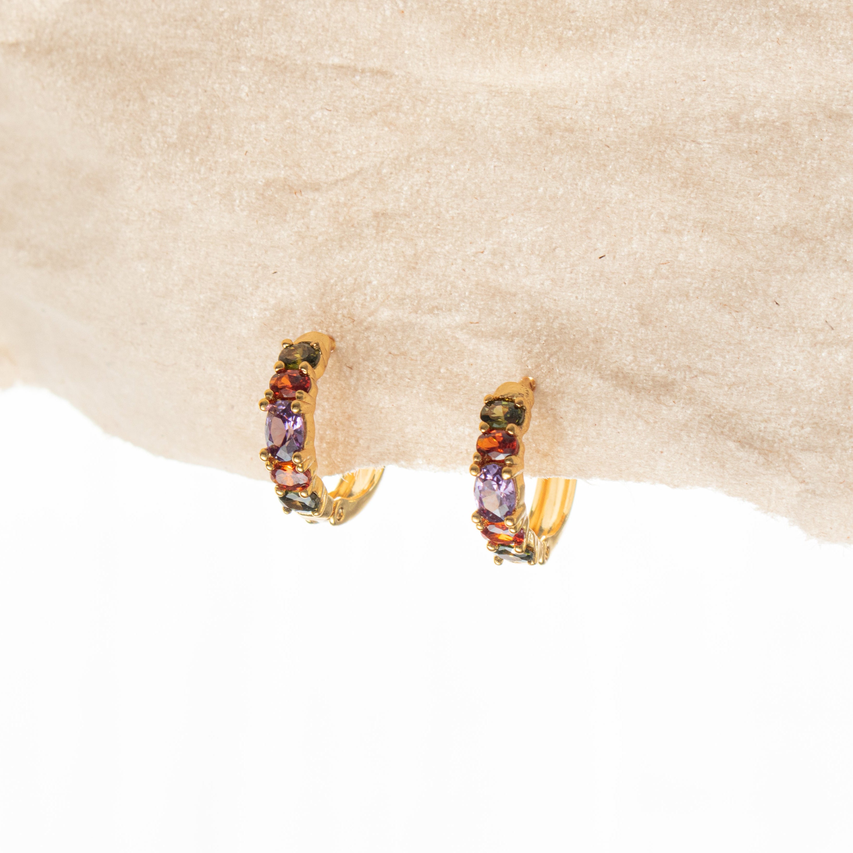 Gold hoop earrings with colorful gemstones on a beige fabric background