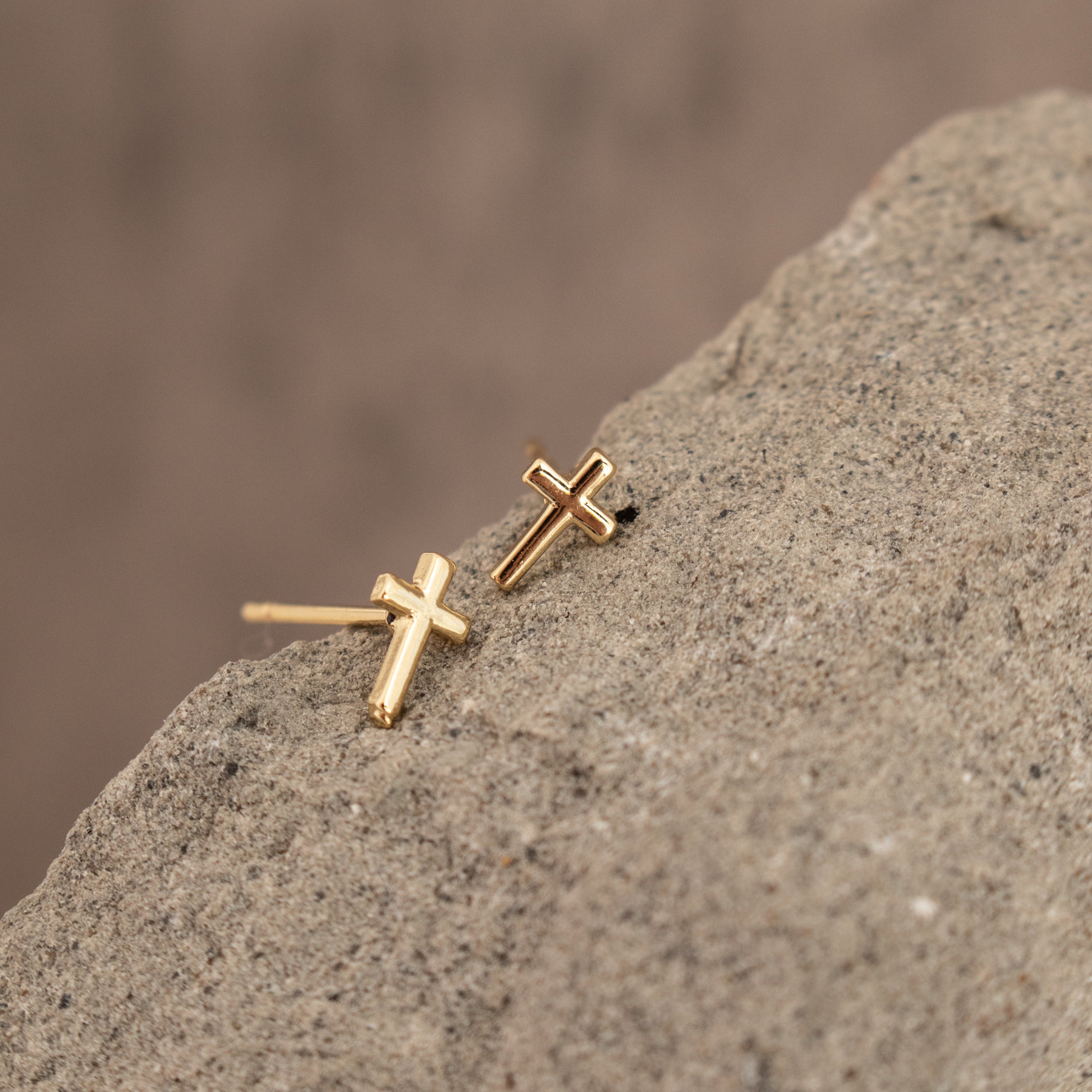 Gold cross earrings on a textured stone surface with a blurred brown background