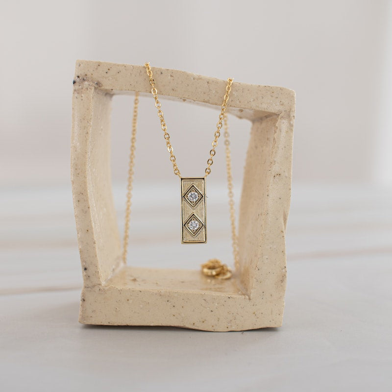 Gold Queen of the Foxes necklace with a double diamond pendant on a ceramic stand against a white background