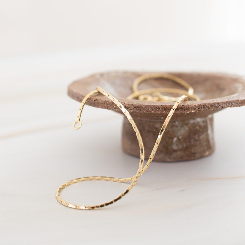 Gold necklace on a wooden stand with a white background