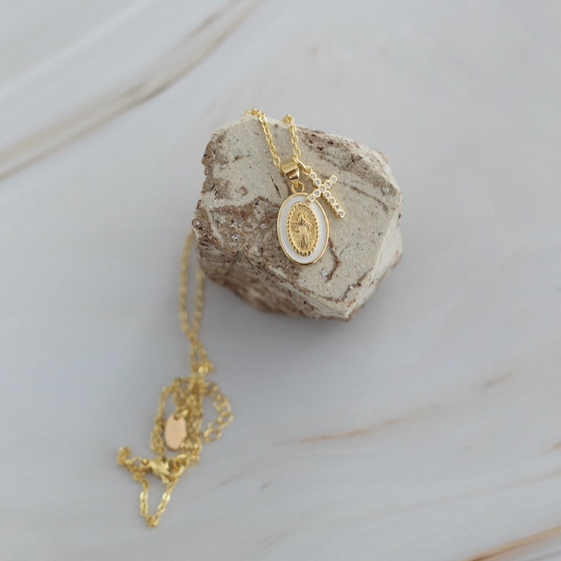 Gold chain necklace with Tiny Mary and Tiny Cross pendants on a textured stone surface