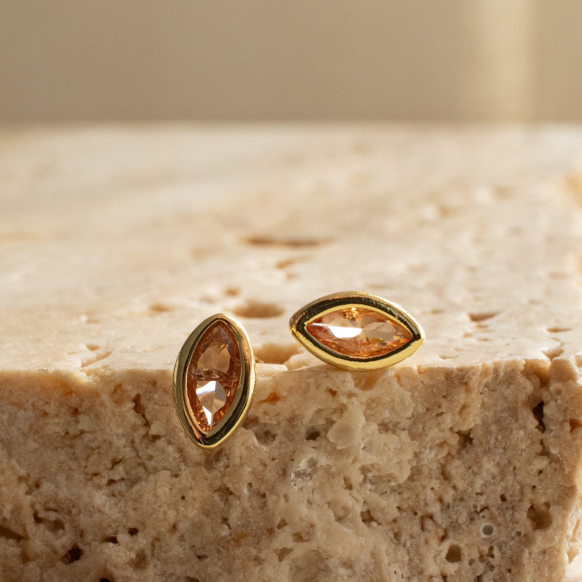 Close-up of two Citrine Marquise Stud earrings on textured stone, showing the faceted stones and smooth gold-plated surrounds.