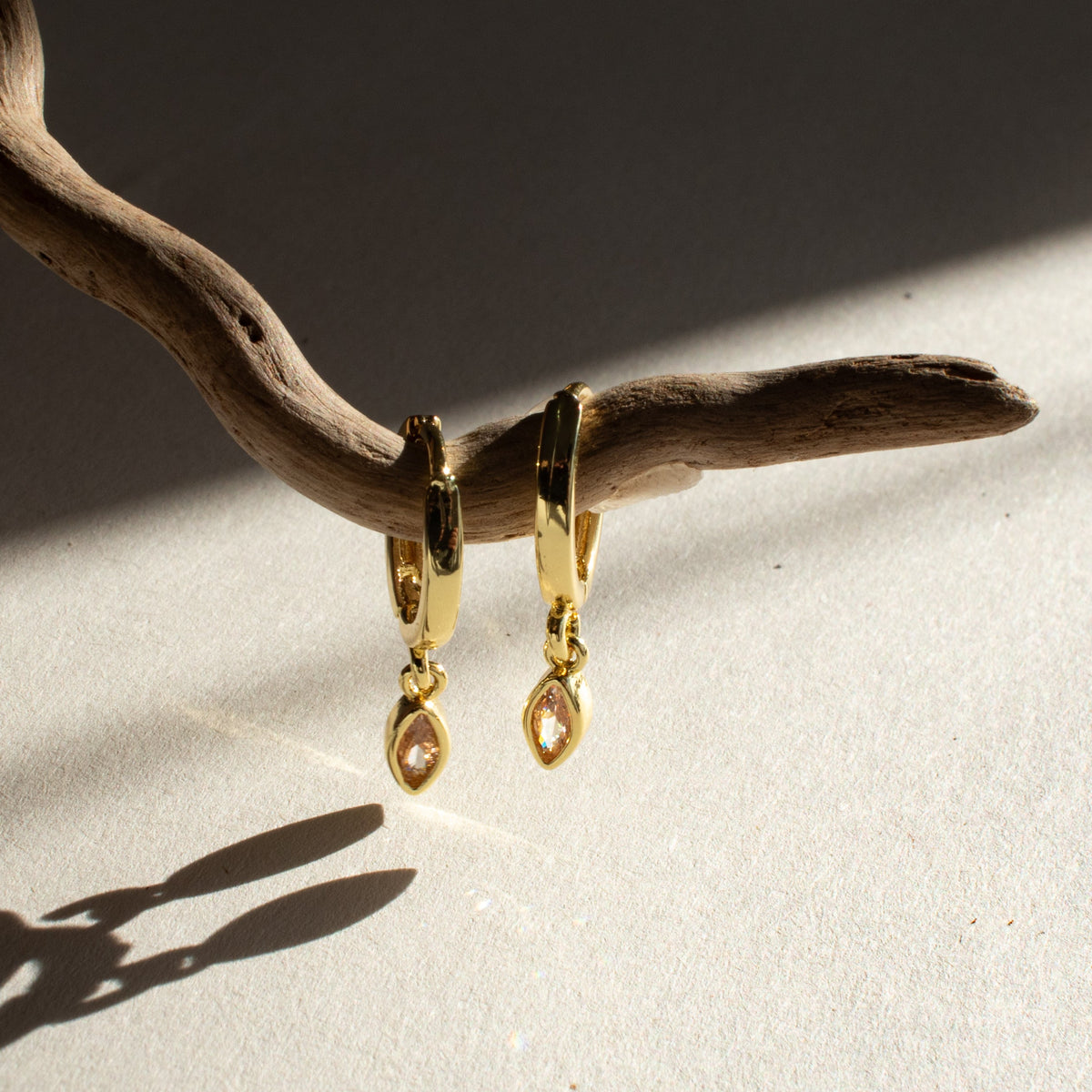Gold-plated Citrine Single Drop earrings with marquise-shaped zirconias hanging from driftwood in sunlight.