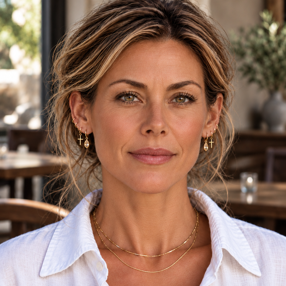 Model in a café wearing Citrine Single Drop earrings in a delicate gold ear stack, with layered necklaces and a white shirt.