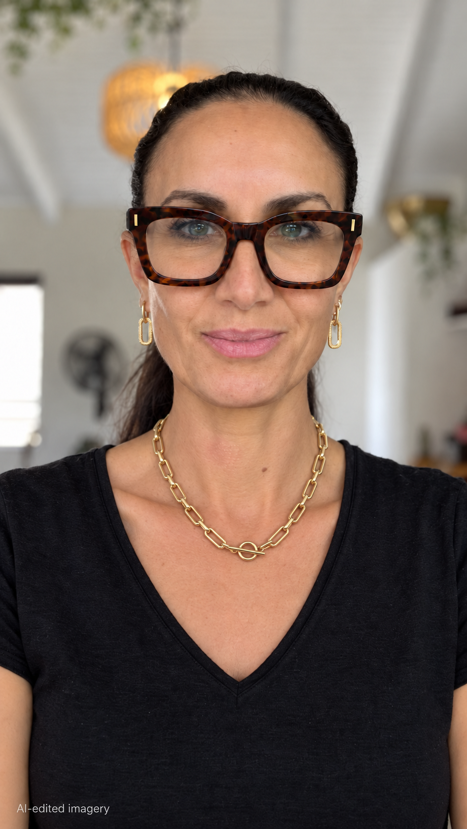 Model in tortoiseshell glasses and a black V-neck top wearing a gold rectangular-link necklace with a front fob clasp.