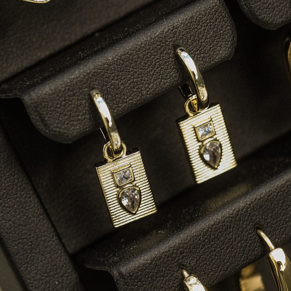 Close-up of gold-plated Dewdrop Sleeper Earrings showing polished hoops, textured rectangular charms and clear cubic zirconias.