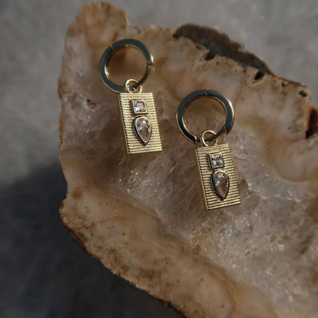 Gold-plated Dewdrop Sleeper Earrings on natural stone, featuring ridged rectangular charms with square and teardrop cubic zirconias.