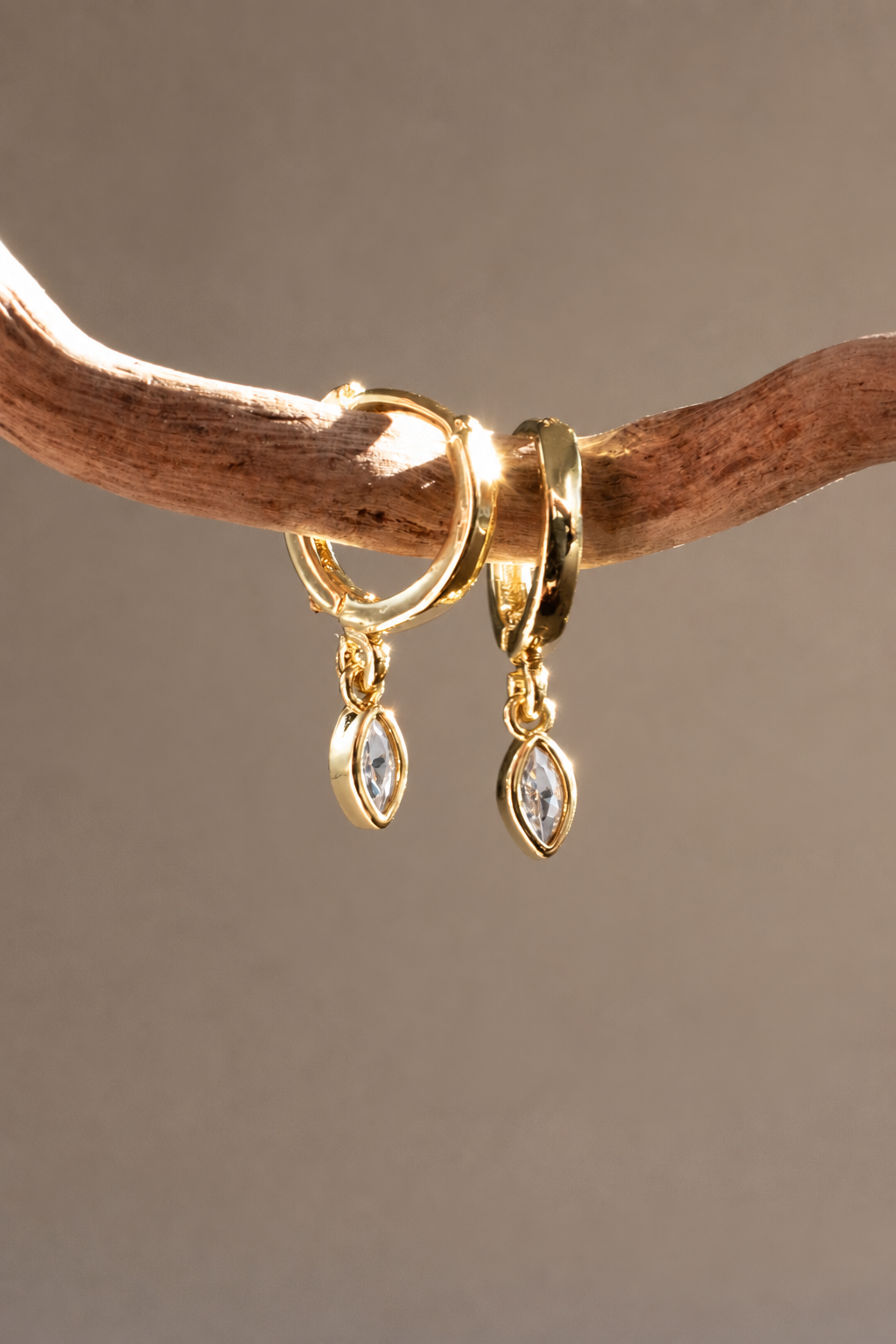 Gold-plated Marquise Single Drop earrings with clear zirconias hanging from driftwood, with sunlight catching the hoops and stones.