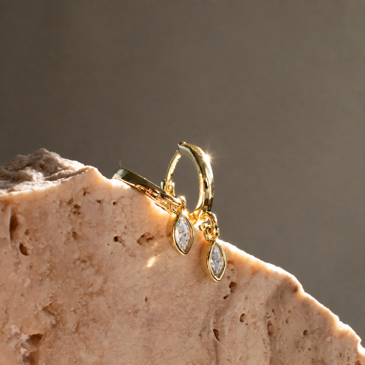 Gold-plated Marquise Single Drop earrings with clear zirconias, displayed on natural stone in sunlight.