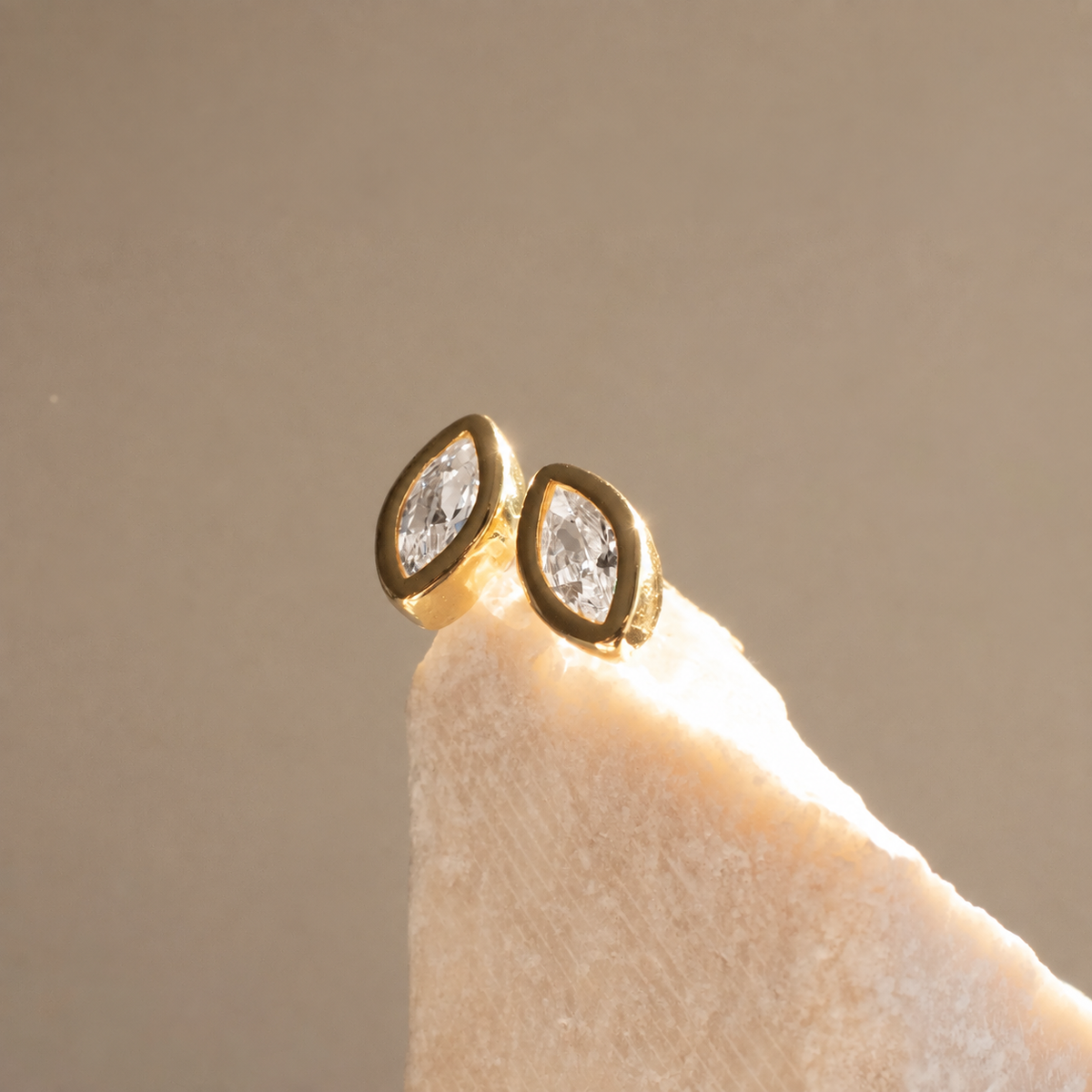 Diamond Marquise Stud earrings with clear zirconias in gold-plated rub-over settings on textured pale stone.