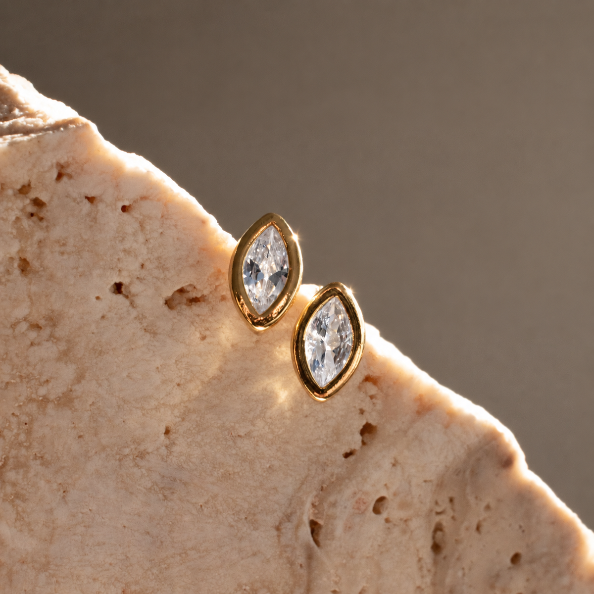 Angled close-up of Diamond Marquise Stud earrings showing faceted clear zirconias and smooth gold-plated settings.