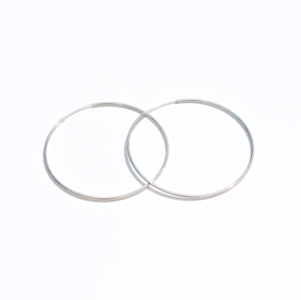 Pair of fine silver hoop earrings overlapping on a white background.