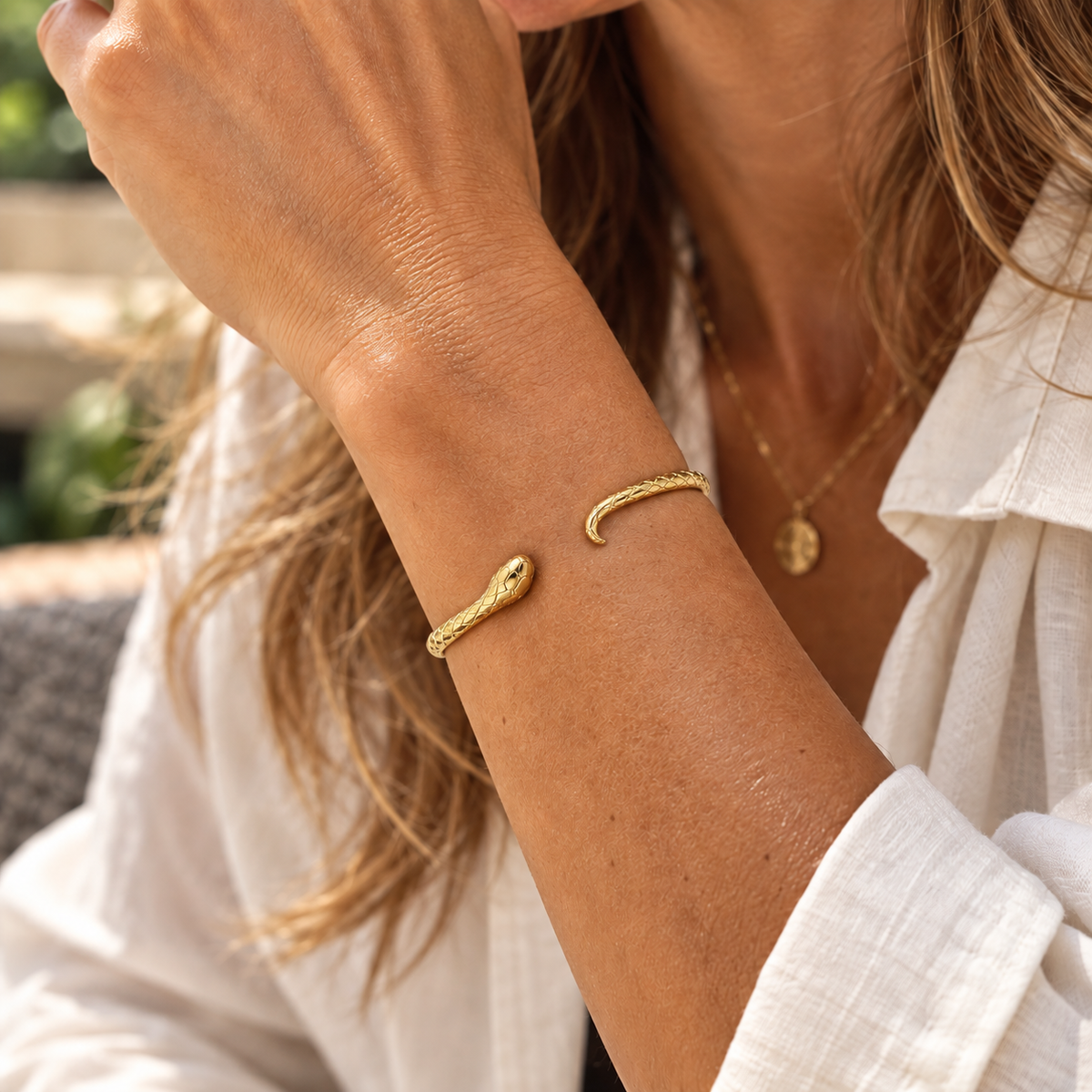 Woman wearing a gold snake cuff bracelet with textured serpent detailing, styled with a white linen shirt and gold jewellery.