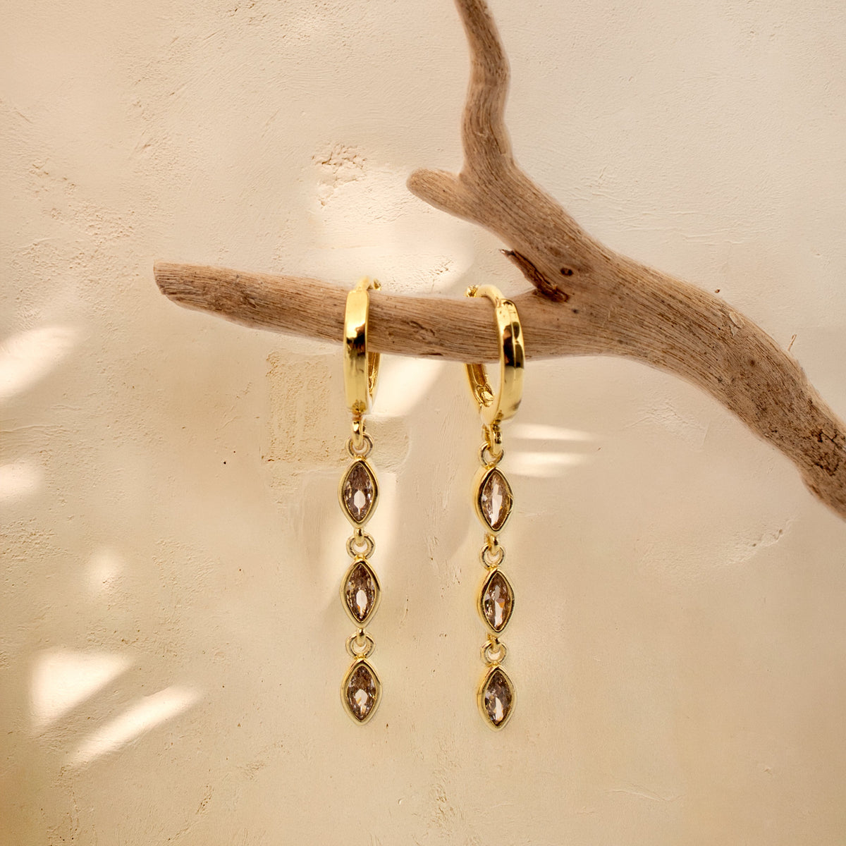 Gold-plated Marquise Triple Drop earrings hanging from a branch, each with three linked marquise-shaped zirconias.