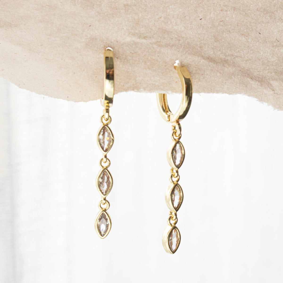 Pair of gold-plated sleeper earrings with three clear marquise-shaped zirconias hanging beneath each hoop against a pale background.