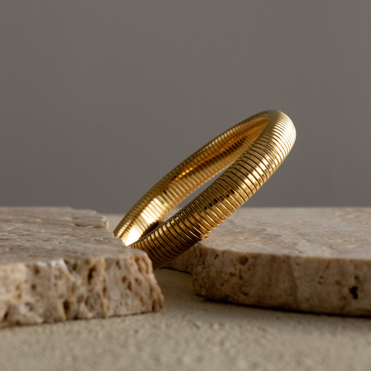 Queen of the Foxes gold-plated Medium Banded Bracelet with a ribbed finish, resting between pale stone pieces.