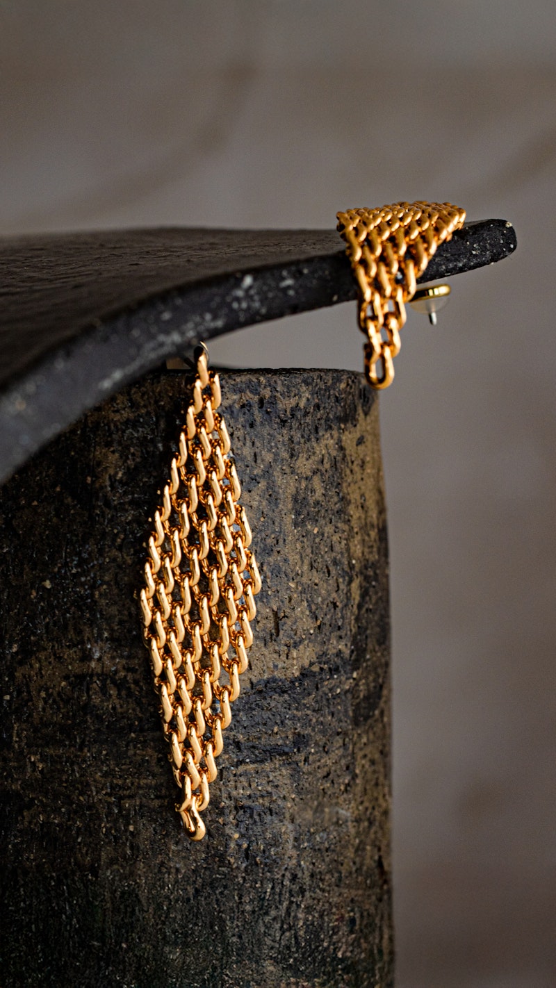 Gold Mesh Diamond Earrings hanging over dark stone, showing their open linked texture and tapered diamond shape.