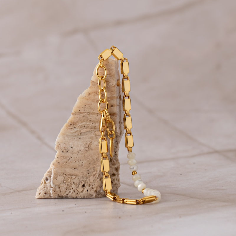 Pearl + Chain Bracelet draped over an upright stone, showing rectangular gold links, faux pearls and an extension chain.