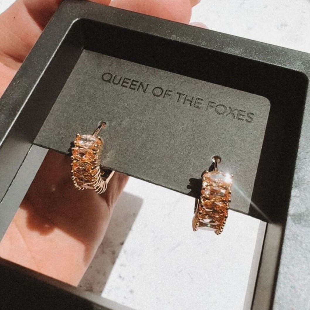 Woman holding Queen of the Foxes gold-plated Perfect Huggie Earrings with Citrine zirconia stones, in packaging.