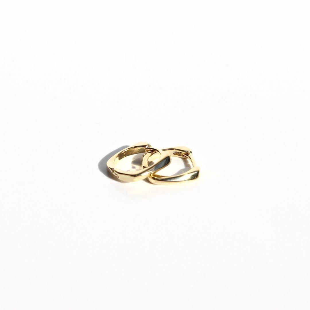 Overlapping petite gold sleeper earrings on a white background, showing their smooth finish and curved shape.