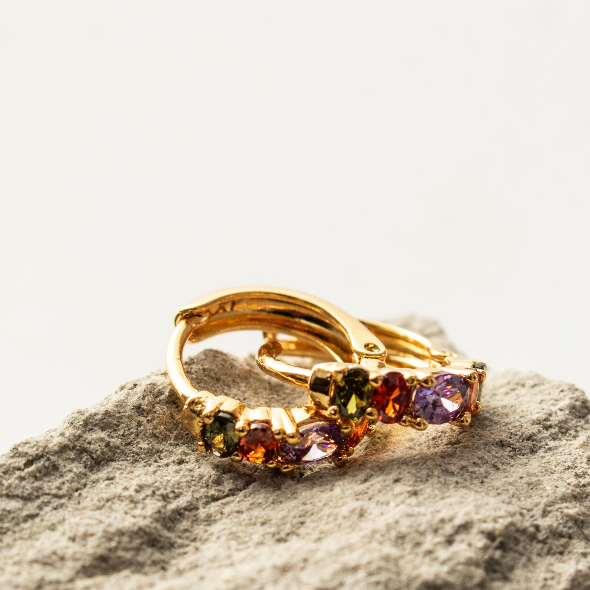 Close-up of Rainbow Sleeper Earrings showing oval coloured zirconias, gold claw settings and hinged hoop fastenings.