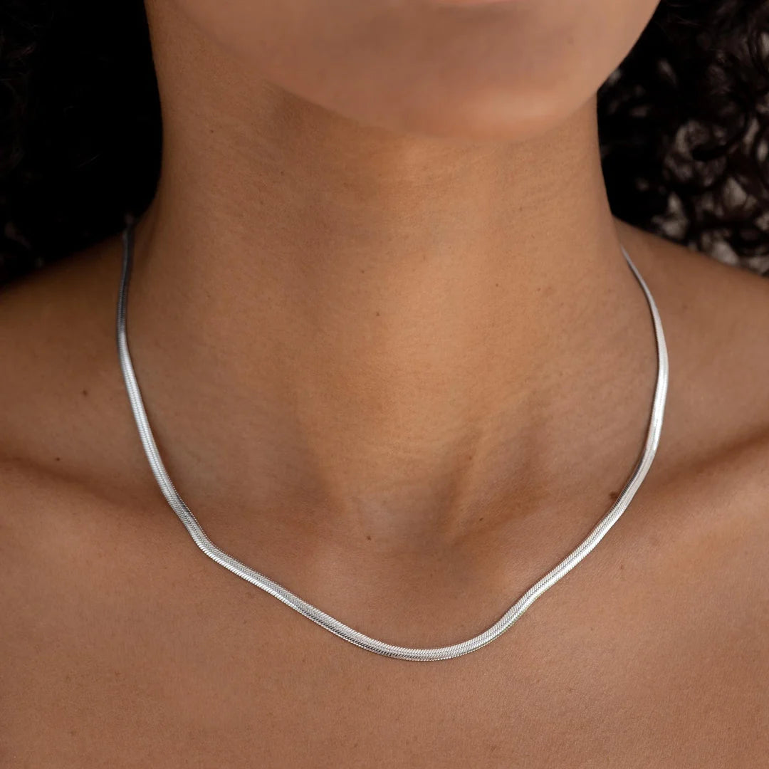 Close-up of a silver herringbone necklace showing its fine, flat links and curved drape around the neckline.