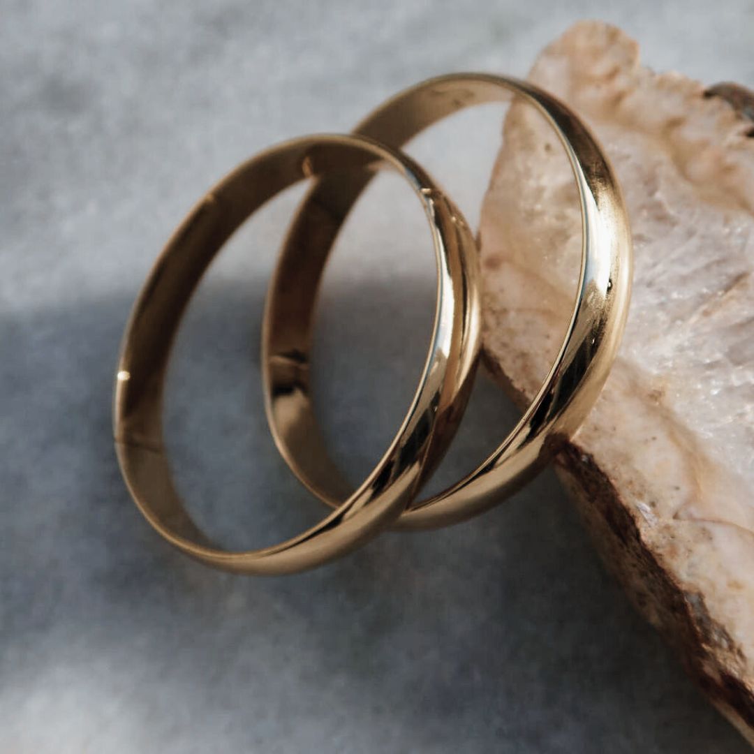 Two Solid Bangles resting against pale stone, showing their smooth gold finish and curved profile.