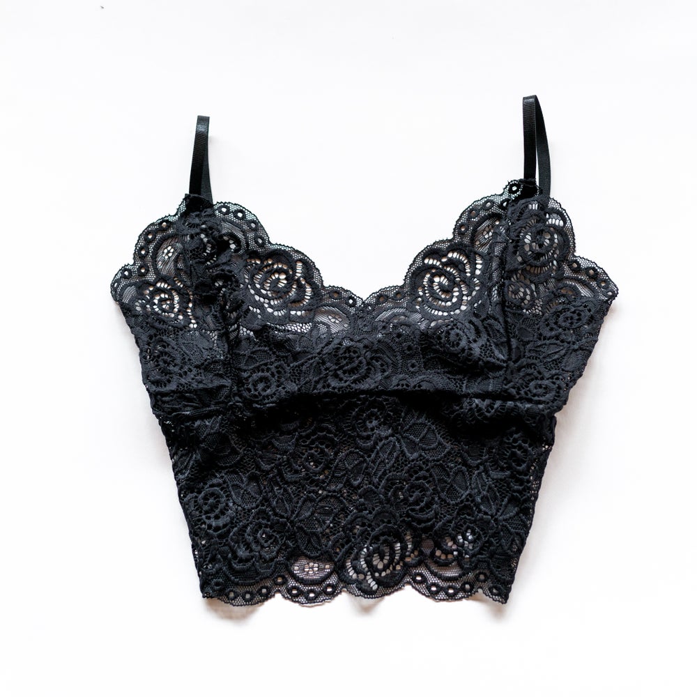 Black longline floral lace bralette with slim shoulder straps and scalloped neckline and hem, laid flat on white.