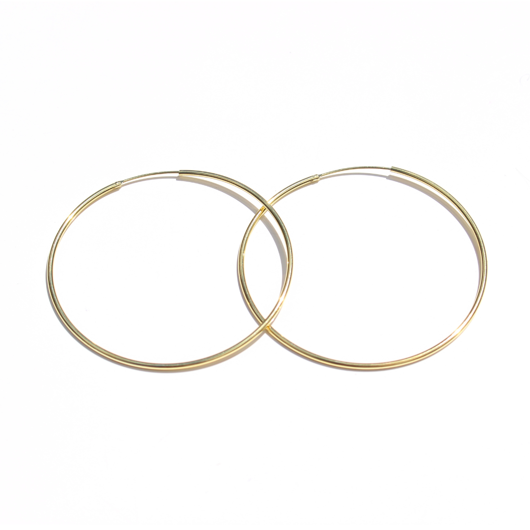 Pair of fine gold hoop earrings overlapping on a white background.