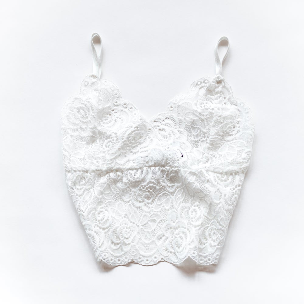 White longline floral lace bralette with slim shoulder straps and scalloped neckline and hem, laid flat on white.